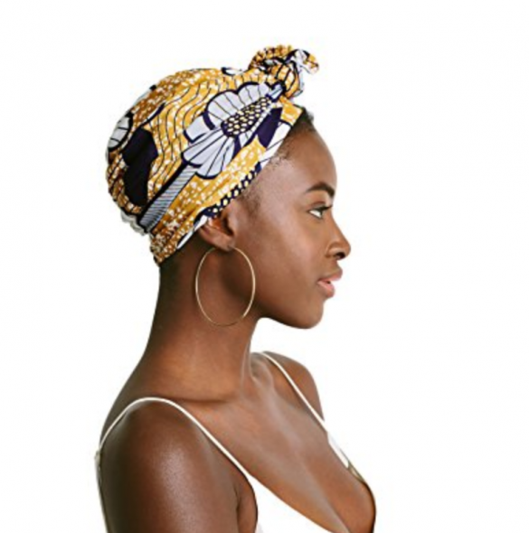 A Black woman in side profile wearing a yellow patterned turban with a tie on the front 