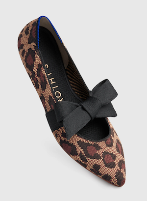 A pointed toe animal print flat with a black fabric ribbon tied over the instep