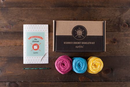 A book, crochet hook and three skeins of yarn against a wooden background