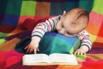 cute baby reading book on colorful background of a multicolored checked blanket