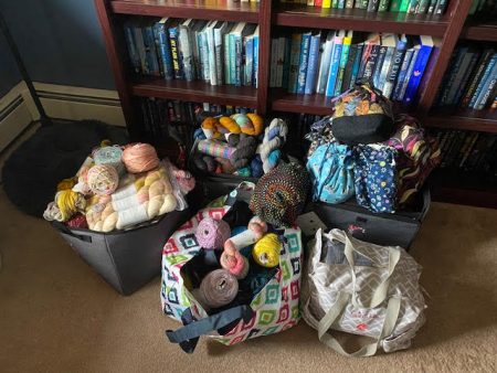 Five totes filled with yarn sitting in front of my bookcase