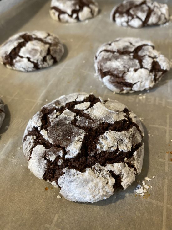 dark chocolate crinkle cookies cooked on a baking sheet with white powdered sugar on the outside 