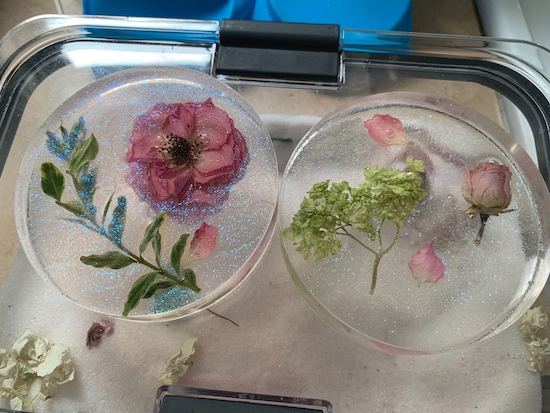 Two round molds of clear resin with flowers embedded inside with a slight iridescent sparkle across the surface