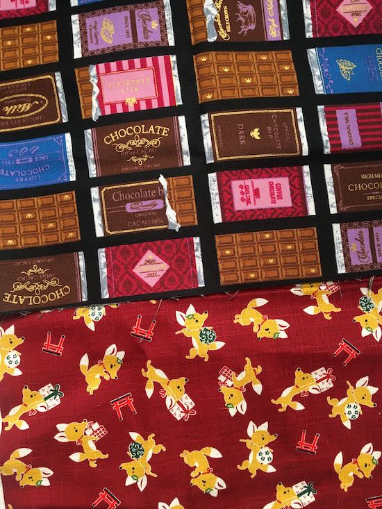Two pieces of fabric, one printed with chocolate bars with multicolored pastel labels marking in a square pattern and the other covered with corgi dogs wearing sweaters