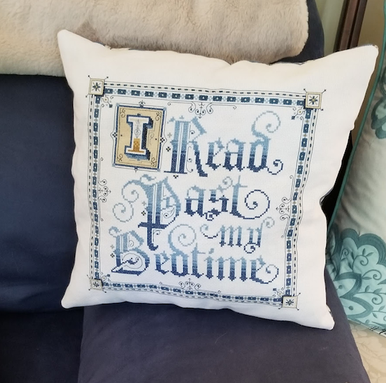 Cross stitched pillow that says I read past my bedtime in blue swirly typography