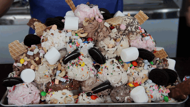 a very very large ice cream sundae of probably fifty scoops of ice cream with toppings like whole cookies whole cones m&ms and sprinkles
