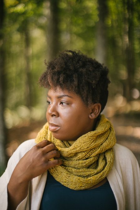 a black woman with short hair models a green cowl with a lacy leaf pattern