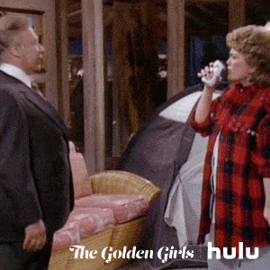Blanche from the Golden Girls spitting out a spray of water. She's wearing a black and red flannel shirt.