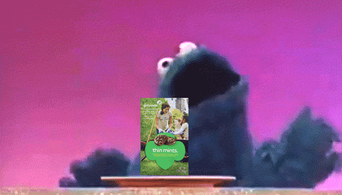 Cookie Monster dancing in front of a purple backgroudn with a box of Thin Mints in front of him