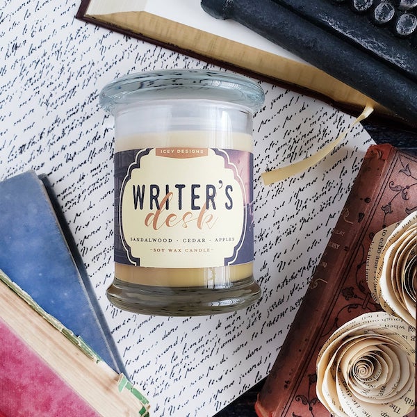 Writers desk candle in a glass jar against a background of written pages and leatherbound books