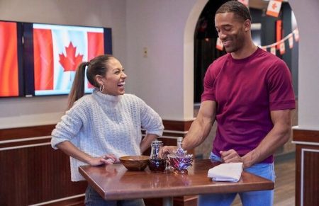 Serena and Matt stand in front of a table with maple syrup on it. A Canadian flag is in the background.