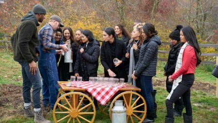 The women stand around a table while a farmer holds up what looks like an old milk jug