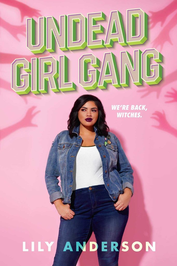 Undead Girl Gang by Lily Anderson. A curvy brown-skinned woman in a denim jacket, black pants, and white tee stands in front of a Barbie pink wall. She's rocking some awesome dark lipstick. The shadows of hands reach out from the edge of the wall toward her.