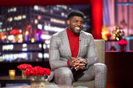 Emmanuel Acho wears a red turtleneck under a plaid suit, and this suit is just painted on over his biceps