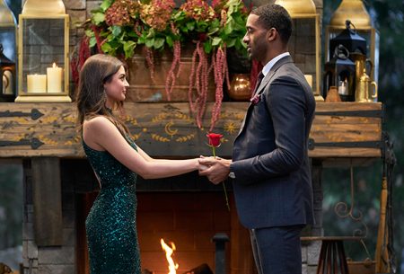 Matt and Rachael hold hands in front of a fireplace