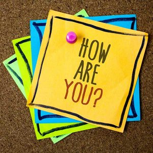 bright green blue and yellow notes with the words HOW ARE YOU? written on the top note held against a bulletin board with a pink pushpin
