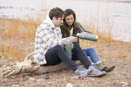 Katie and Greg sit on a log and drink from a thermos