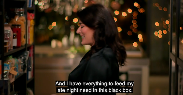 A screen grab of Nigella in black shiny pajamas looking at her pantry shelf and saying I have everything I need to feed my late night need in this black box.