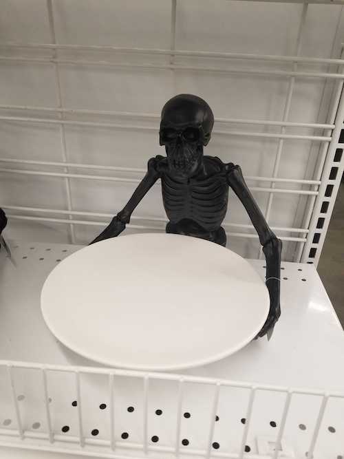 A black plastic skeleton holding a shallow bowl with its arms