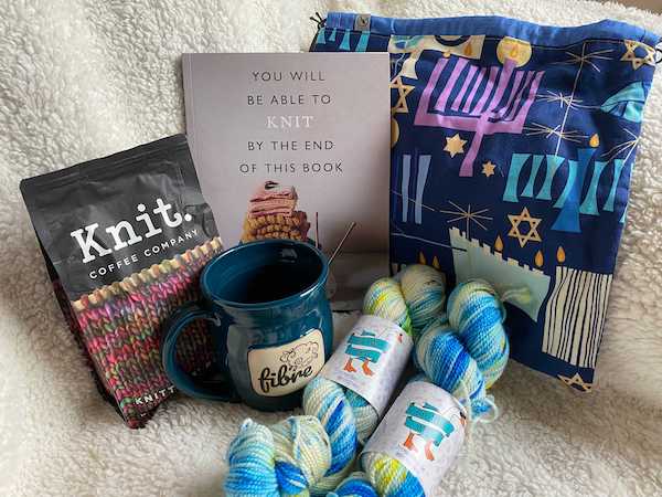A set of books, a Hanukkah craft bag yarn and coffee and a mug on a white fleece backdrop