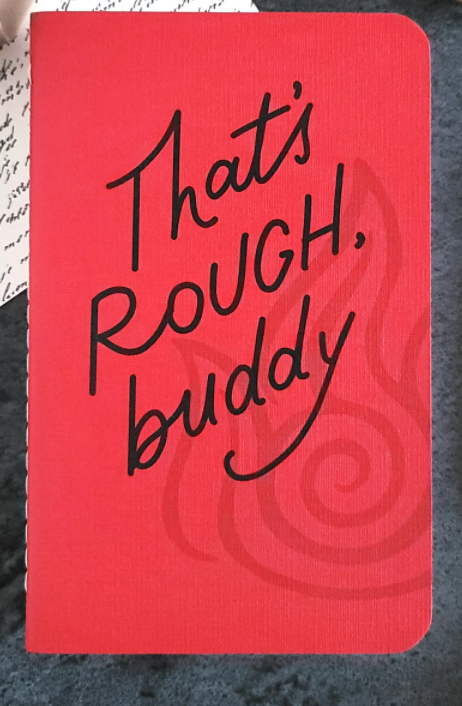 A red notebook with the words That's Rough Buddy from Avatar