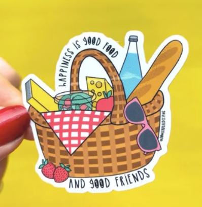 An illustrated sticker with a picnic basket filled with bread, wine, water, cheese and a book with the caption Happiness is good food and good friends