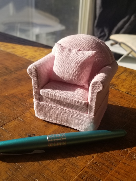 a pink fabric easy chair with a curved back and a little pink fabric pillow on the seat