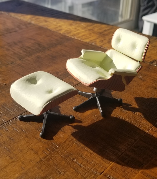 A dollhouse Eames chair and footrest in carved plastic with a very light green painted seat and cushions