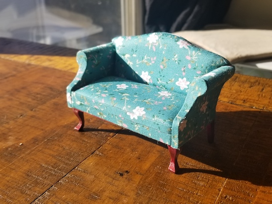 A miniature dollhouse sofa with a curved back and carved legs in a teal floral print