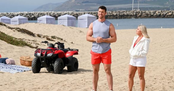 Clayton in red swim trunks standing on the beach again looking baffled maybe that's just his face? 