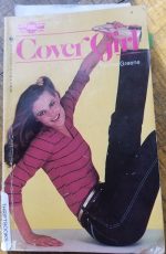 A photograph of a book with a model in a red striped shirt holding her foot flexed above her she's wearing metallic gold shoes, belt and scrunchie too