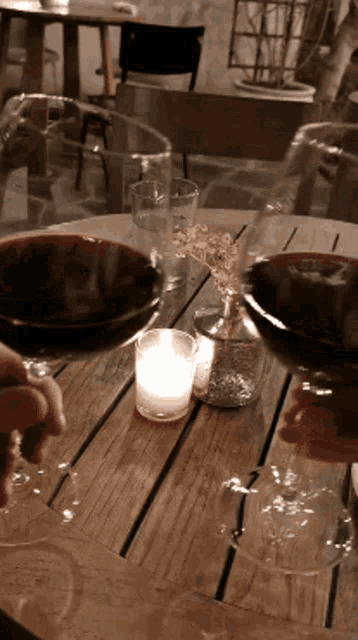 a looped gif of two large glasses of red wine clicking together with a votive candle in the background