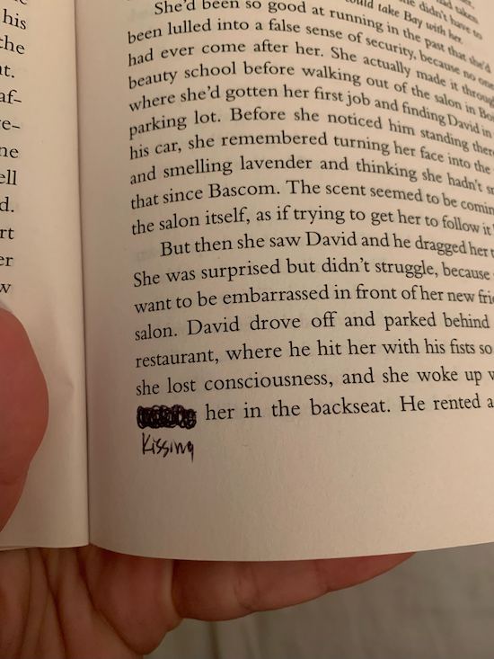 A close up of the text of a book where the word fucking has been scratched out and replaced with kissing