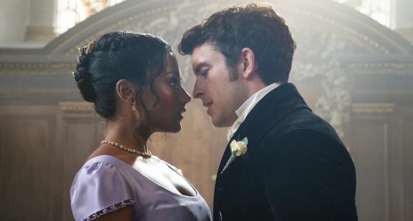 Kate and Anthony almost kiss in a church. She is wearing a violet gown and he's wearing a black overcoat, cravat and boutonniere, and their noses are probably 5mm apart