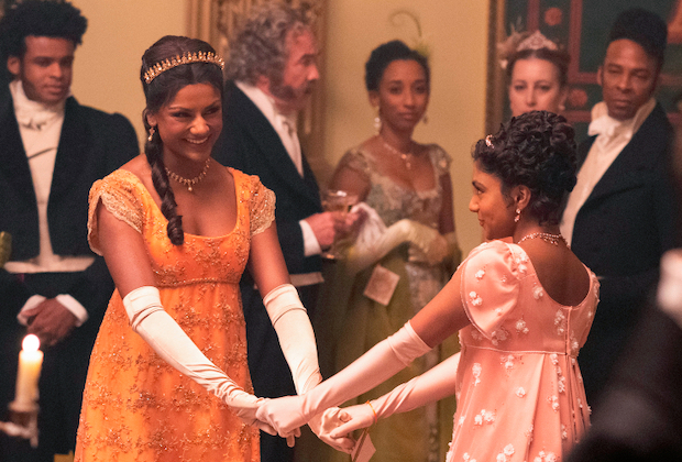 Kate and Edwina kick up their heels at a ball. Kate is holding Edwina's hands in a bright orange gown and tiara, and edwina is in a very vivid rose pink