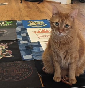 An Orange tabby sits on a t shirt quilt in progress laid out on the floor