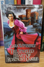The Jeweled Heart of Rosemont Castle by Clara Wimberly. A dark haired woman in a fuchsia and black dress is running through the hills, away from a castle.