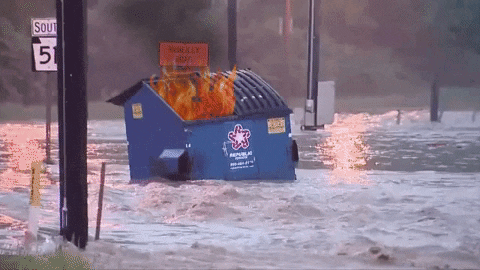A dumpster on fire floating down a flooded roadway