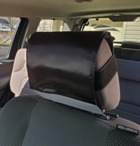 A photo of a car head rest with a satin hair shield wrapped around the front and top with elastic bands on the sides.