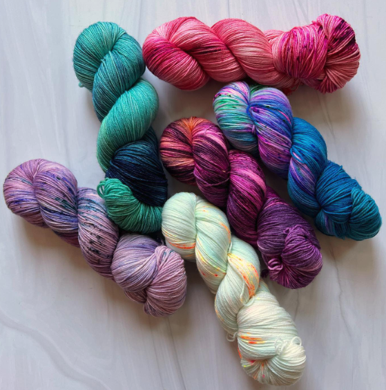 A picture of the six colourways for Romancelandia: one green, one purpe, one mint, one deep violet, a dark blue and a magenta on a white marble tabletop