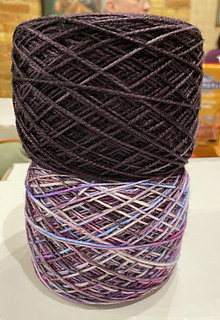 A skein of purple yarn over a skein of variegated yarn
