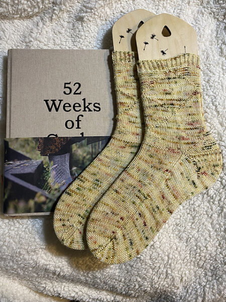 A pair of variegated yellow socks next to the book 52 Weeks of Sockse