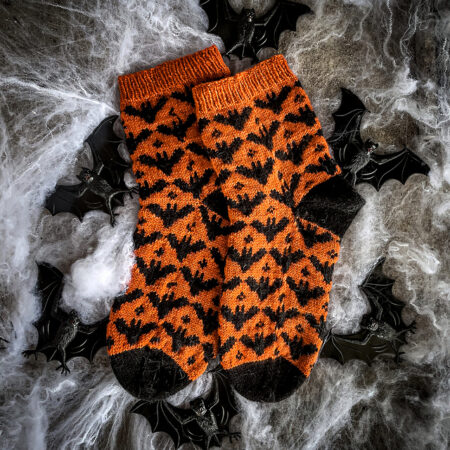 A pair of orange socks with black bats throughout, black heels and black toes