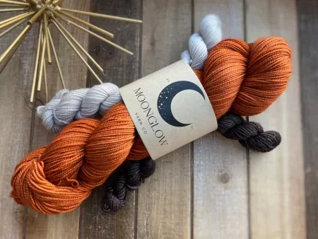 A skein of orange yarn with white and black mini skeins