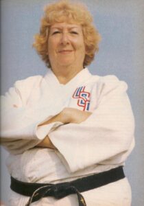 Color photograph of Rusty in a USA judo uniform with short blonde wavy hair and a smile with her arms crossed she looks very strong