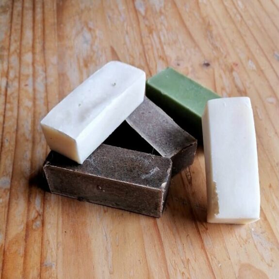 A small stack of bars of soap in white, brown, and green on a wood table.