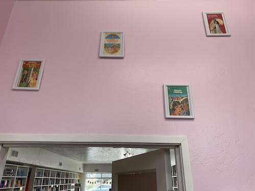 A pink wall with a high ceiling and white windowbox frames of some classic category romances and covers
