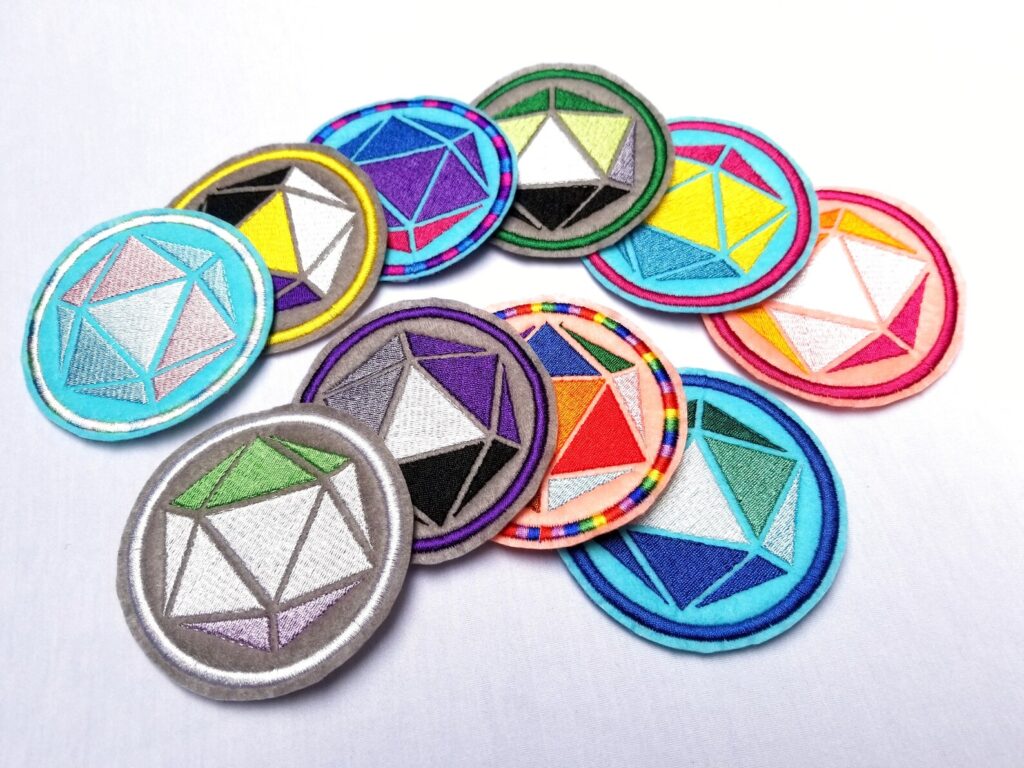 Pride d20 patches. An assortment of patches with d20 dice in pride flag color schemes.
