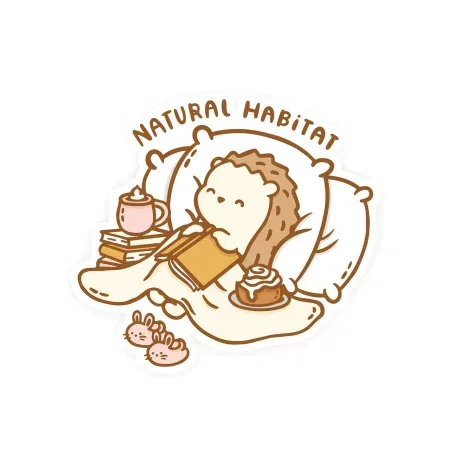 A hedgehog sleeps in bed surrounded by books, tea and a cinnamon roll. The words 'natural habitat' are on top