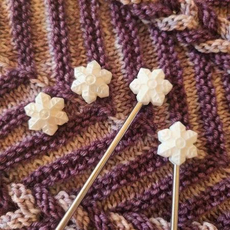 White stitch stoppers shaped like snowflakes against a background of a purple knitted shawl or scarf